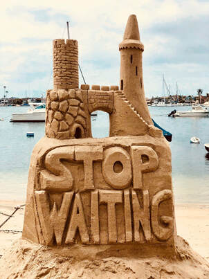 Background, port with boats and sea. Foreground, beach with sandcastle on top of sand base with words 